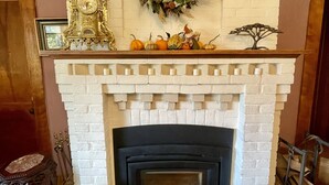 A fireplace with a white brick surround, a decorative wreath above it, and a mantelpiece with pumpkins and a small tree ornament.
