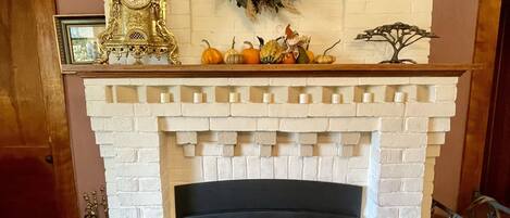 A fireplace with a white brick surround, a decorative wreath above it, and a mantelpiece with pumpkins and a small tree ornament.