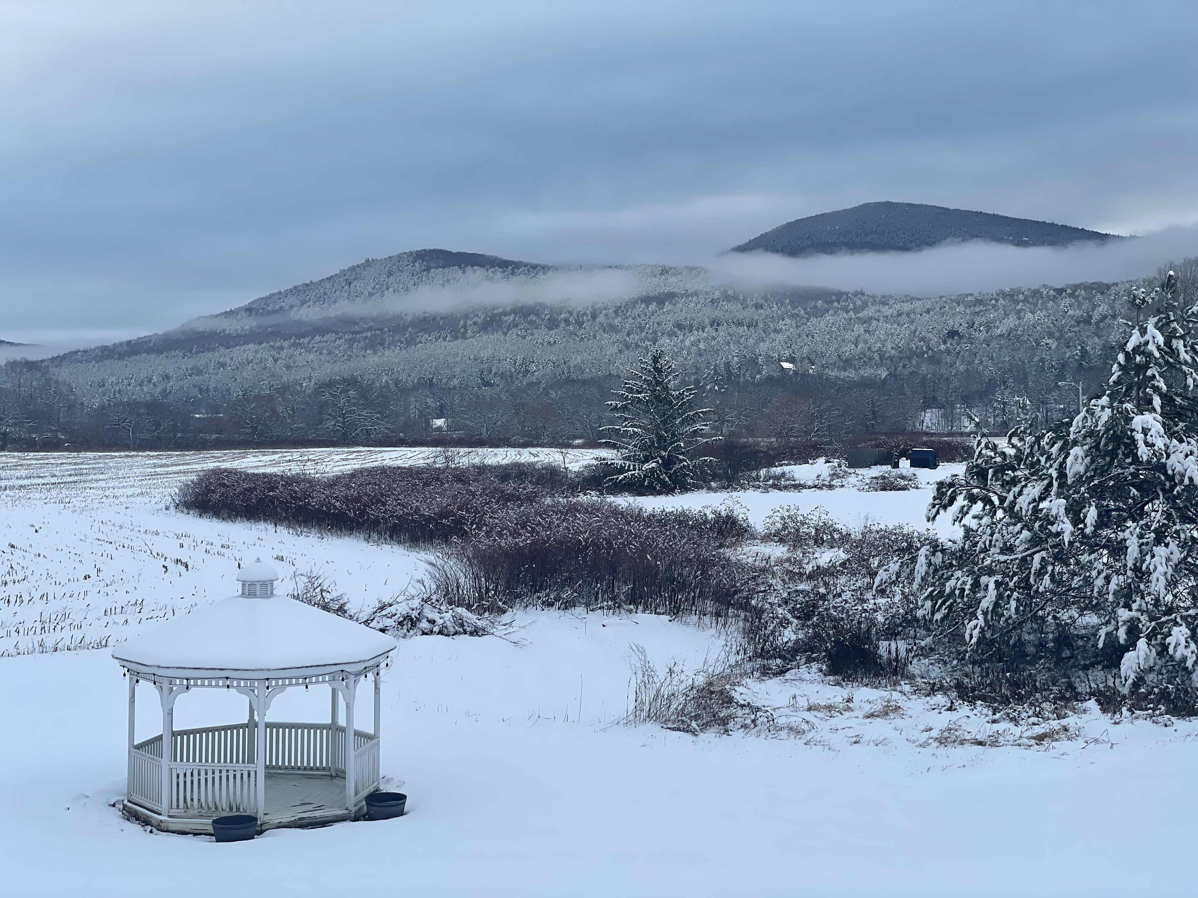Een prieel in een besneeuwd landschap met bergen op de achtergrond.