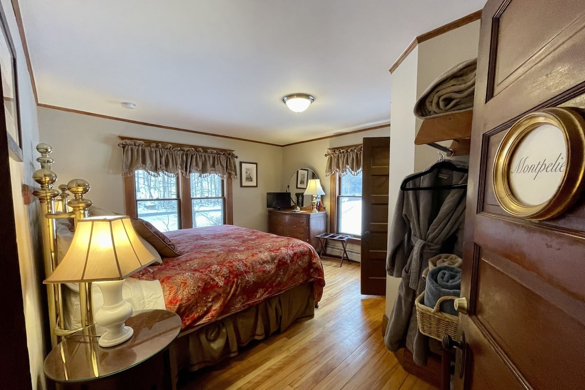 A bedroom with a bed, bedside table with lamps, a dresser, and a coat rack.