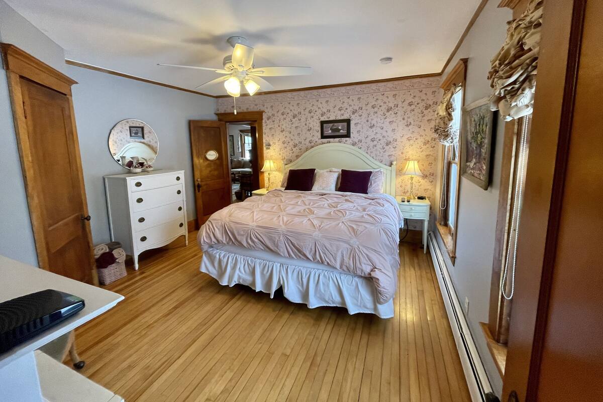 A bedroom with a bed, a dresser, a mirror, a ceiling fan, and a nightstand with a lamp.