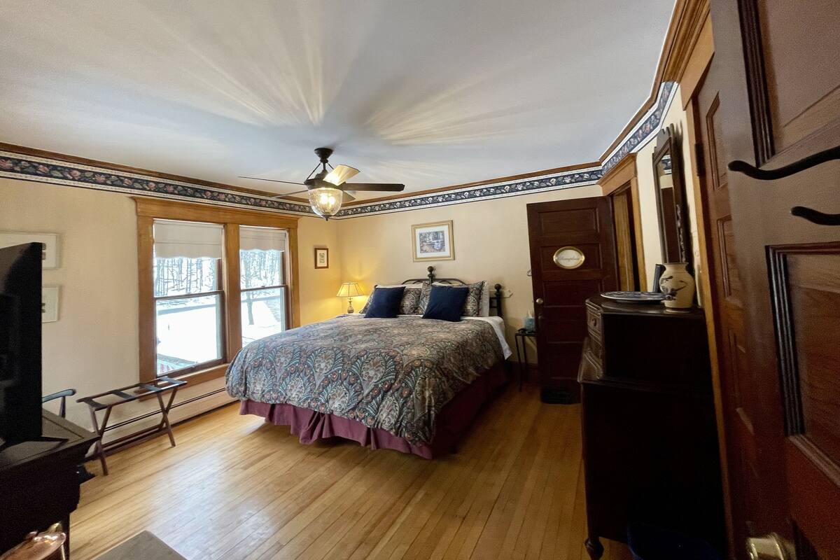 A bedroom with a bed, a ceiling fan, a window, and a door.
