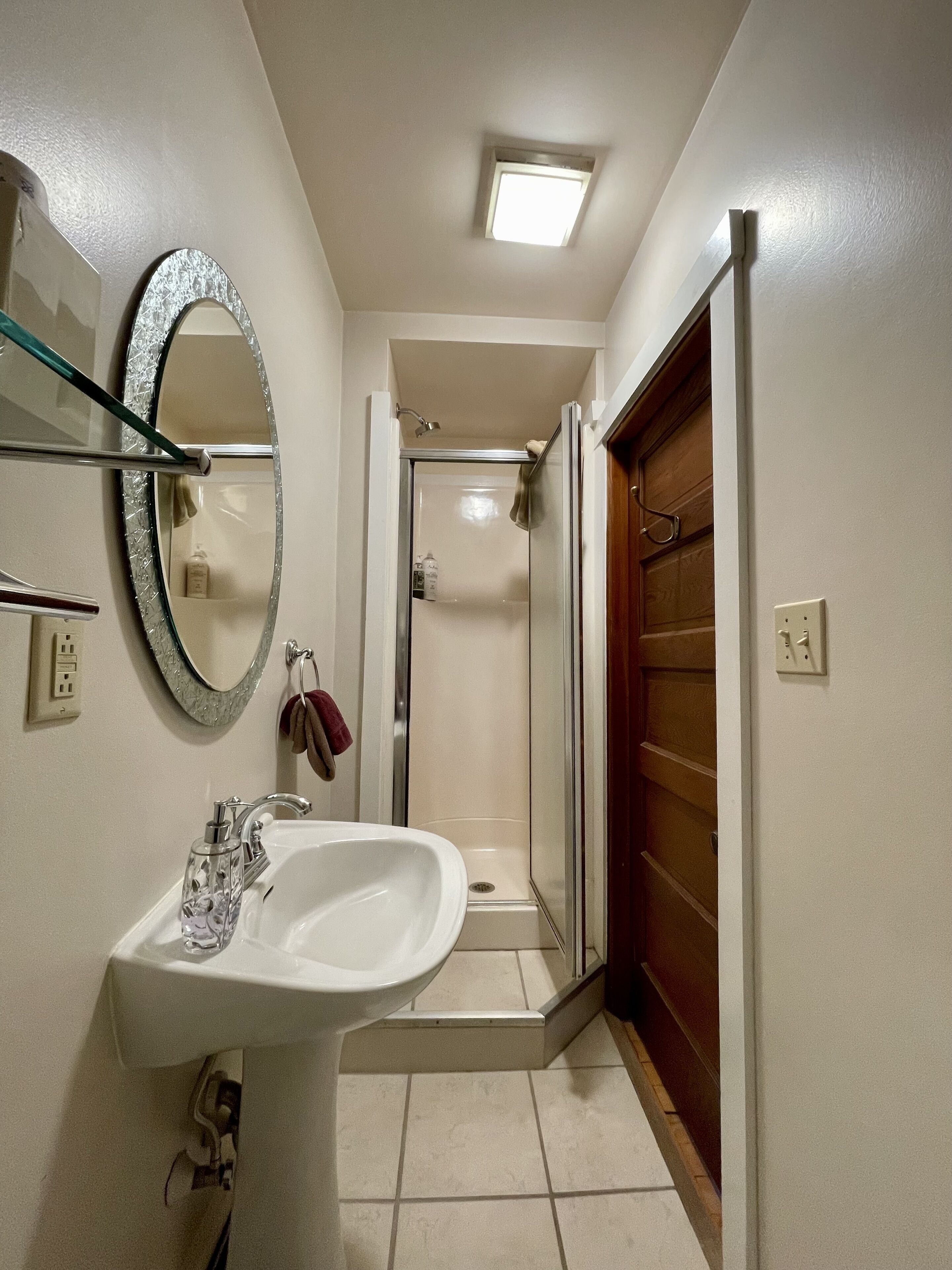A bathroom with a white sink, a glass shower enclosure, and a wooden door.
