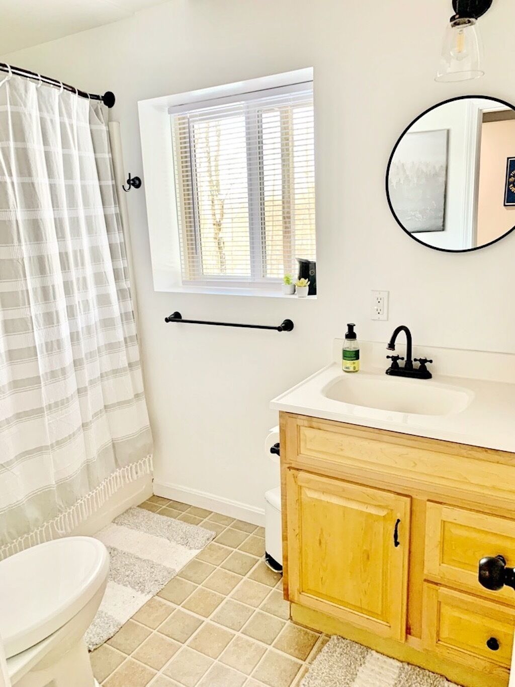 A bathroom with a toilet, a sink with a mirror, a window with blinds, and a shower curtain.