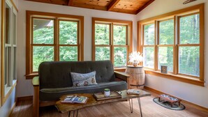 Una habitación acogedora con techo de madera, ventanas amplias, un sofá, una mesita de café y un rincón para alimentar a mascotas.