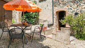 An outdoor dining area with a table and chairs, an orange umbrella, and a stone building in the background. - Beautiful apartment in villa for 4 people with WIFI, pool, TV, patio and pets allowed (Casole D'elsa)