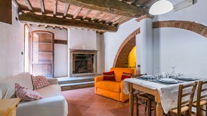 A cozy living room with a fireplace, a dining table set for four, and a sofa with a checkered pillow. - Beautiful apartment in villa for 4 people with WIFI, pool, TV, patio and pets allowed (Casole D'elsa)