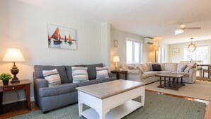 Ein Wohnzimmer mit grauem Sofa, weißem Couchtisch und grauem Teppich. An der Wand hängt ein Gemälde und auf dem Nachttisch steht eine Lampe.