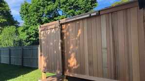 Eine Holzterrasse mit weißer Basis, umgeben von einem Holzzaun und üppigen, grünen Bäumen.