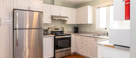Features a kitchen with stainless steel appliances, white cabinetry, and a wooden floor.