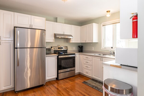 Features a kitchen with stainless steel appliances, white cabinetry, and a wooden floor.