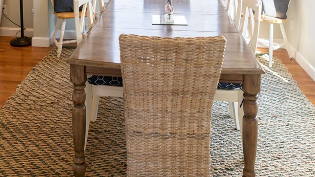 Ein Essbereich mit Holztisch, Korbstühlen, einer Chandelüstere und Blick durch eine Glastür.