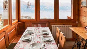 Ein Esszimmer mit Holzboden, einem Tisch für vier Personen, großen Fenstern und Bergblick.