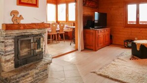 Ein gemütliches Blockhaus-Interieur mit Kamin aus Stein, Holzwänden, einer Essecke und einem Fernseher.