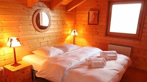 Ein gemütliches Schlafzimmer in einer Holzhütte, mit einem Bett, zwei Nachttischlampen, einer Kommode und einem Fenster.