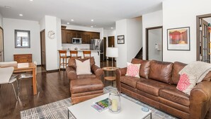 Un salon moderne avec un canapé en cuir marron, une table basse blanche et un coin repas comprenant une table et des chaises en bois.