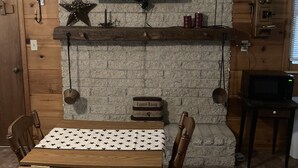 Een eetgedeelte met een schouw van baksteen, een televisie erboven en een tafel met stoelen.