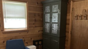 Een kamer met houten wanden, een blauwe fauteuil, een passende voetenbankje, een kast met decoratieve panelen en een raam met jaloezieën.