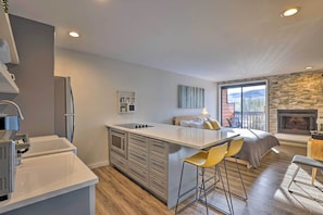 A modern kitchen with a central island, bar stools, a fireplace, and a large window with a view.