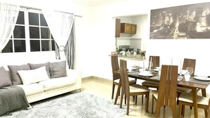 Ein Wohnzimmer mit einer Couch, einem Esstisch mit Stühlen und einer Küche im Hintergrund.