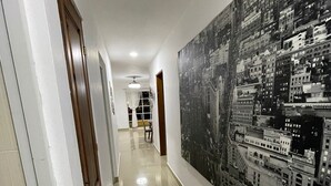 Ein Flur mit großem Stadtbild-Wandgemälde an der rechten Wand, einer Holztür links und einem Fliesenboden.