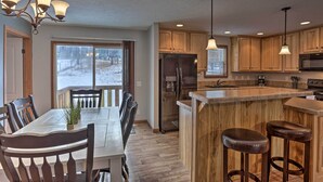 A modern kitchen with wooden cabinets, a large island with stools, a built-in refrigerator, and pendant lighting.