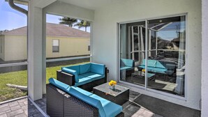 A covered patio with wicker furniture, a glass door leading to a backyard, and a view of a neighboring house.