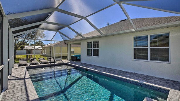 A swimming pool with a covered area, clear blue water, and a patio with lounge chairs.