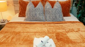 Una cama bien hecha con una colcha marrón, dos almohadas estampadas y una toalla doblada con un alfiler decorativo.