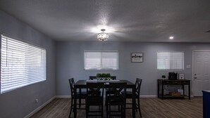 A dining area with a table and chairs, a ceiling light, and a small table with a plant and a coffee maker. - Charming 3 Bedroom residential home with parking on site. (El Paso)