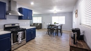 A modern kitchen with stainless steel appliances, blue cabinets, and a dining area with wooden chairs and a table. - Charming 3 Bedroom residential home with parking on site. (El Paso)
