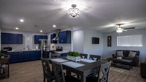 A modern kitchen with dark blue cabinets, a central island, and a dining area with a table and chairs. - Charming 3 Bedroom residential home with parking on site. (El Paso)