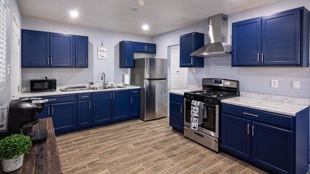 A modern kitchen with blue cabinets, stainless steel appliances, and a wooden floor. - Charming 3 Bedroom residential home with parking on site. (El Paso)