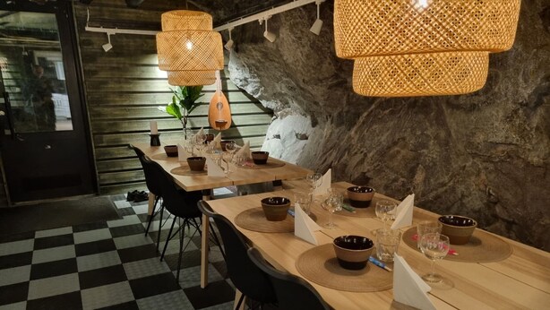 Un restaurante con suelo de cuadros, mesas de madera, sillas negras e iluminación de fibra trenzada.