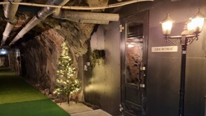 Una entrada temática de cueva con un letrero que dice 'CAVE RETREAT', follaje artificial y un felpudo.