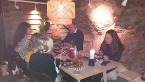 Un grupo de personas cenando en una mesa con un centro de mesa de velas, rodeado de paredes de piedra y una lámpara colgante.