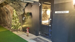 Entrada a un refugio en cueva con un tapete que dice 'Bienvenido', un árbol de Navidad y una decoración de reno.