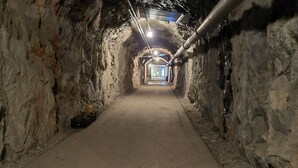 Un túnel con paredes de piedra y suelo de hormigón, que conduce a una zona bien iluminada al final.
