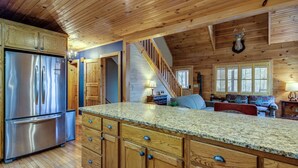 A spacious kitchen with wooden cabinets, a stainless steel refrigerator, and a granite countertop. - Blowing Rock Cabin | Hot Tub, Fire Pit, Fall Views (Blowing Rock)