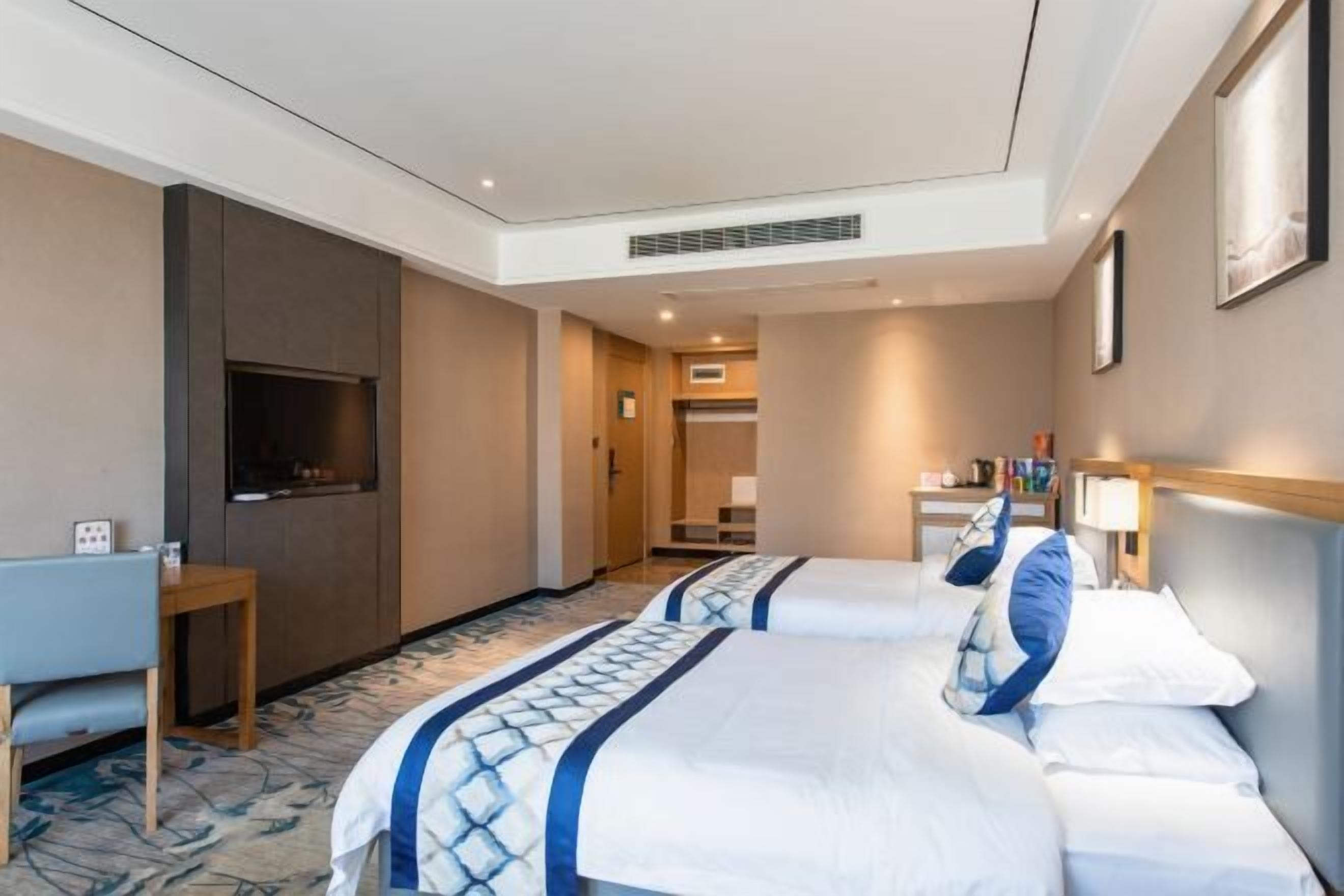 Une chambre d’hôtel avec deux lits, un bureau, une télévision et une salle de bain visible à travers une porte ouverte.