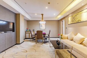Una habitación de hotel moderna con televisión de pantalla plana, un comedor con mesa y sillas, un sofá y un elemento decorativo en la pared.
