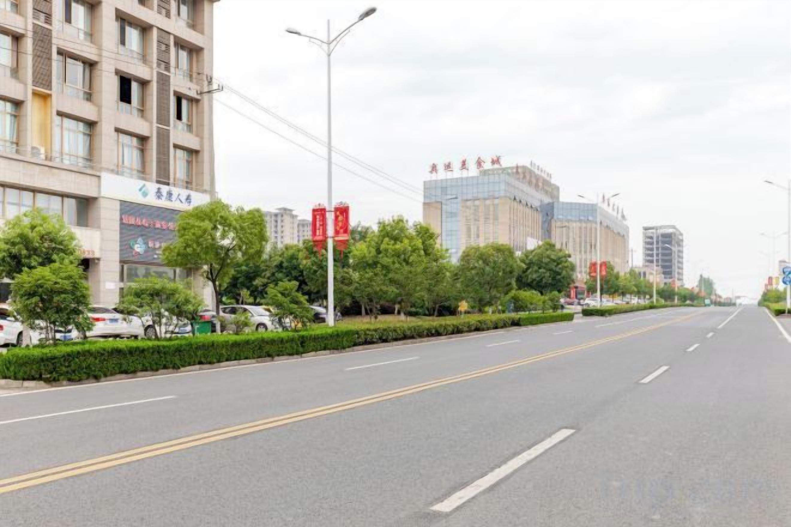 A wide, empty road with buildings on the left and a clear sky.