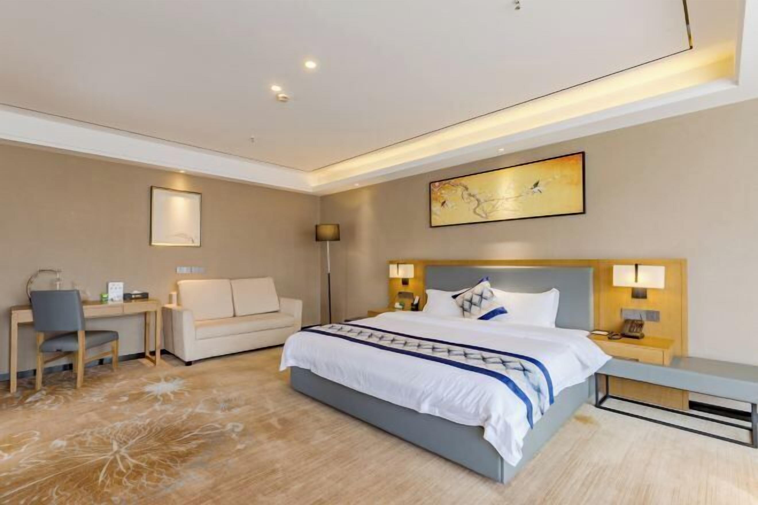A modern hotel room with a bed, desk, chair, and a painting on the wall.