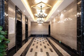 A corridor with a patterned floor, a chandelier, and marble walls.
