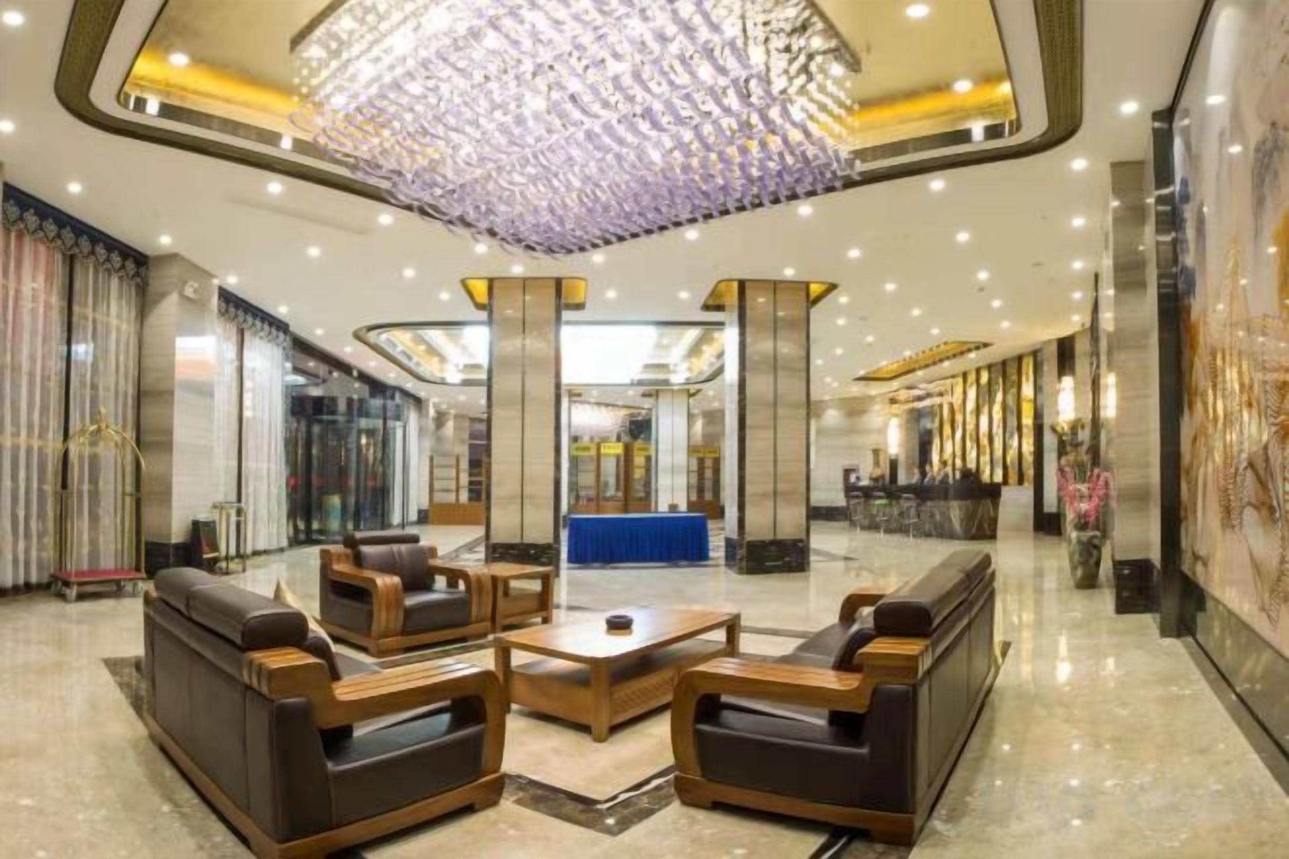 A lobby with a chandelier, seating area, reception desk, and a large mirror.