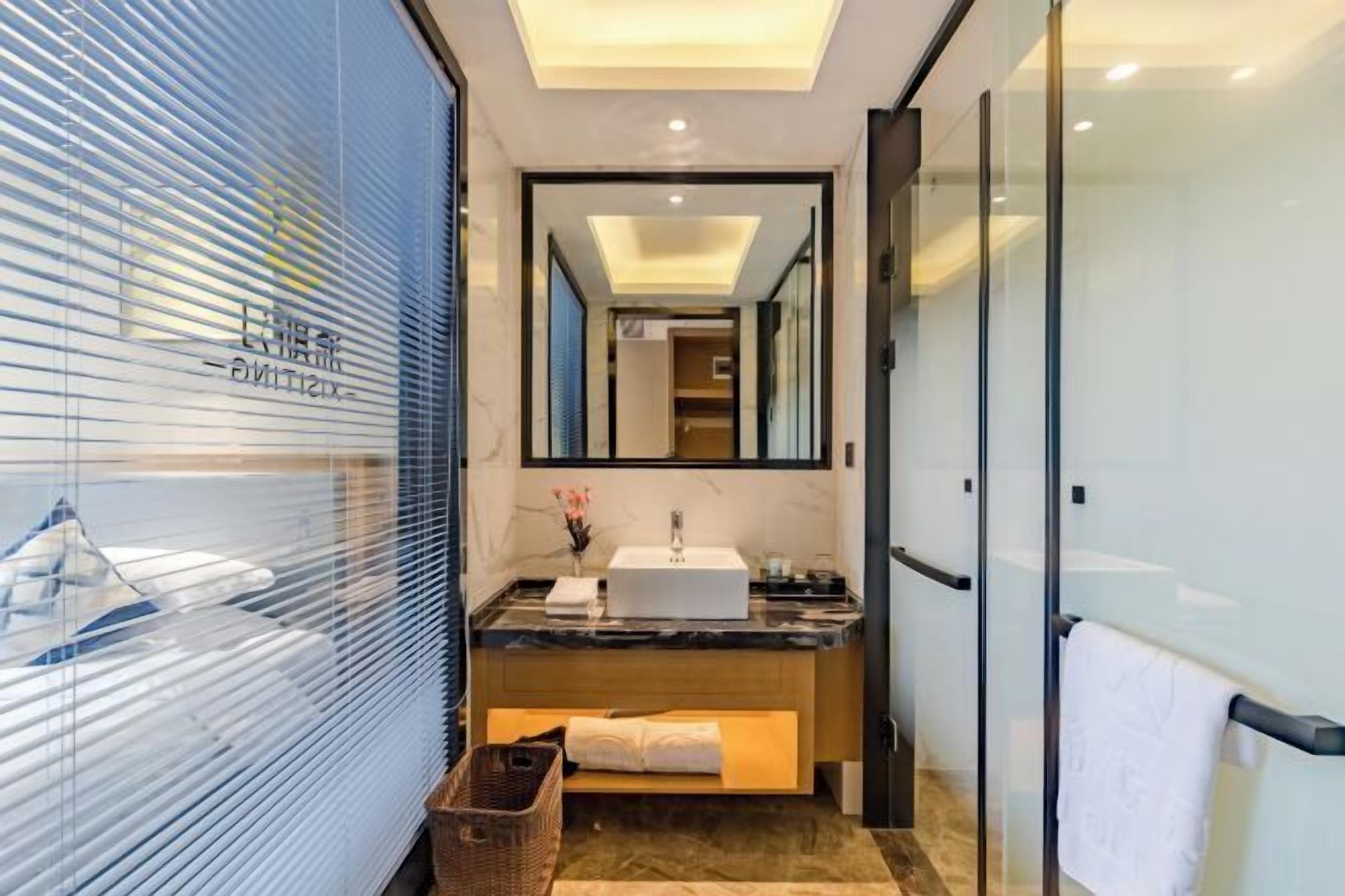 A modern bathroom with a large mirror, a white sink, and a wooden vanity.