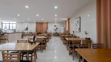 A spacious dining area with multiple wooden tables and chairs, a bar counter, and artwork on the walls.