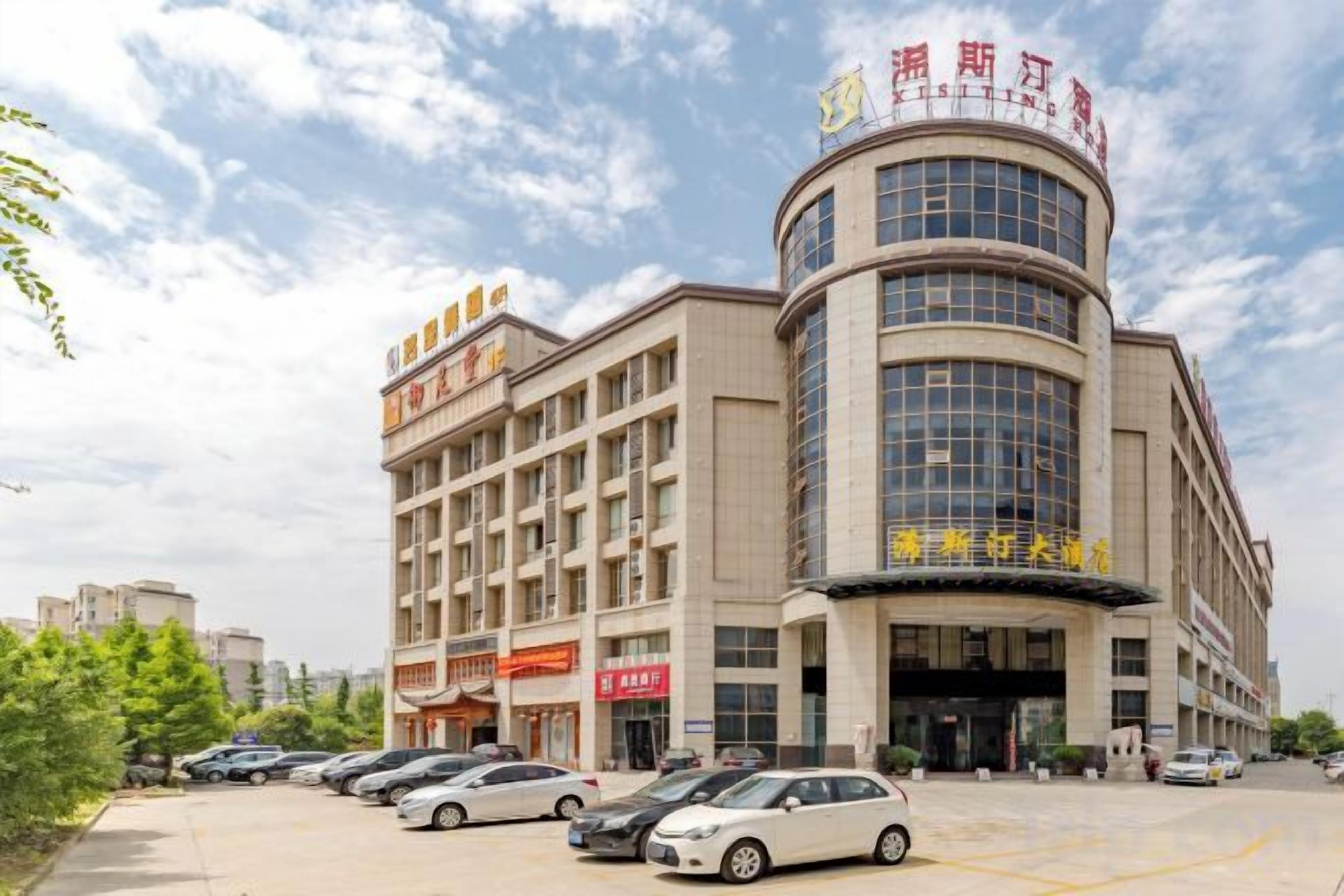 A multi-story building with a curved facade, multiple balconies, and a parking lot with several cars.
