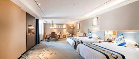 Habitación de hotel con dos camas, una zona de estar con una mesa y sillas, y un ventanal grande.