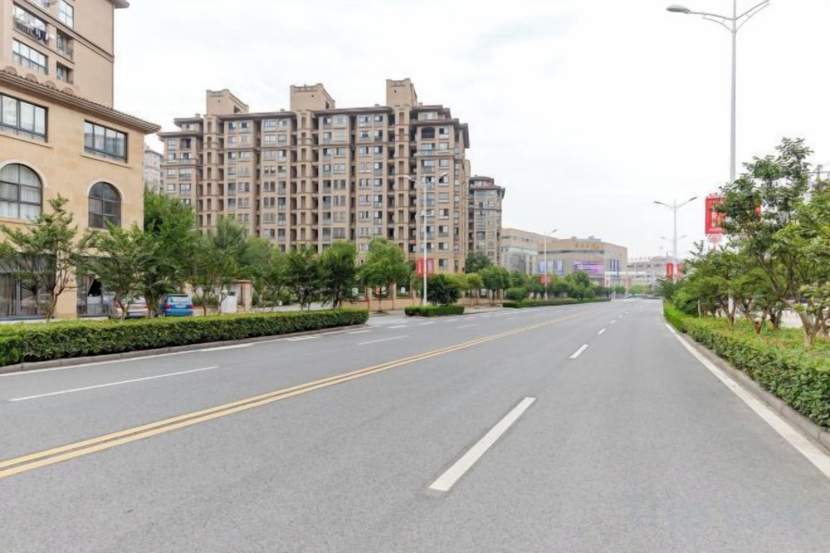 A multi-story residential building with a flat facade, a wide road with a median strip, and street lamps.